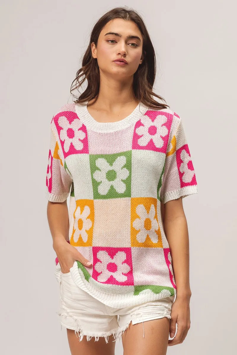 Woman wearing a colorful checkered sweater with flower patterns on a plain background