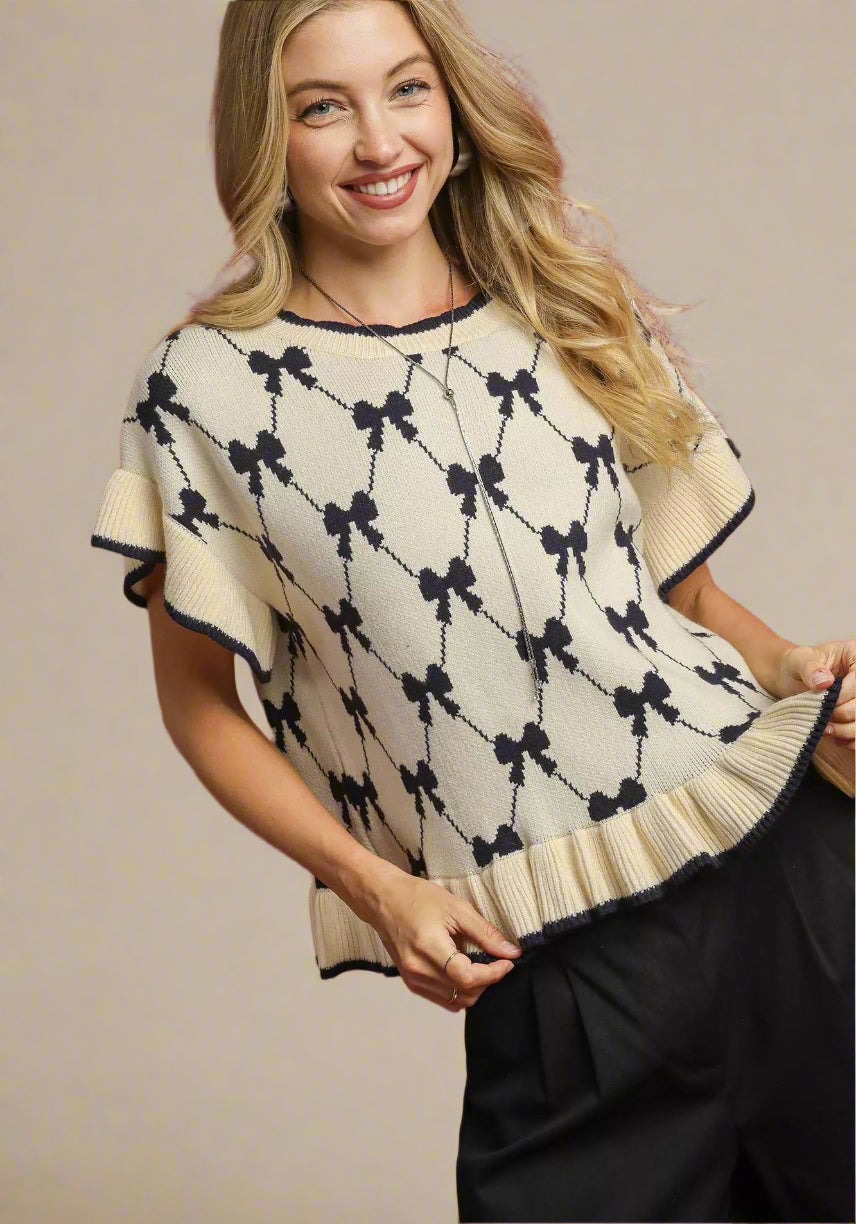 Woman wearing a cream sweater with black bow pattern against a red background