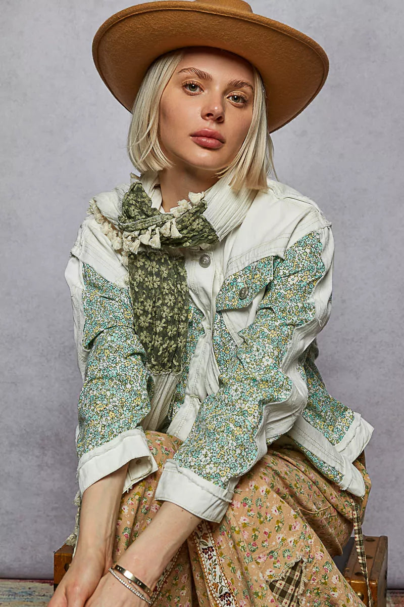 Person wearing a floral jacket, beige hat, and patterned scarf against a gray background
