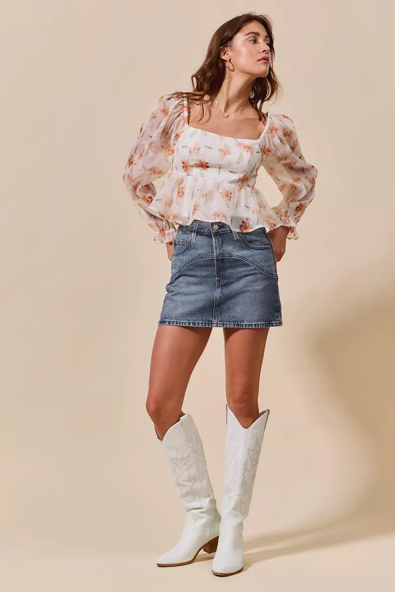 Woman wearing a floral blouse, denim skirt, and white cowboy boots against a beige background