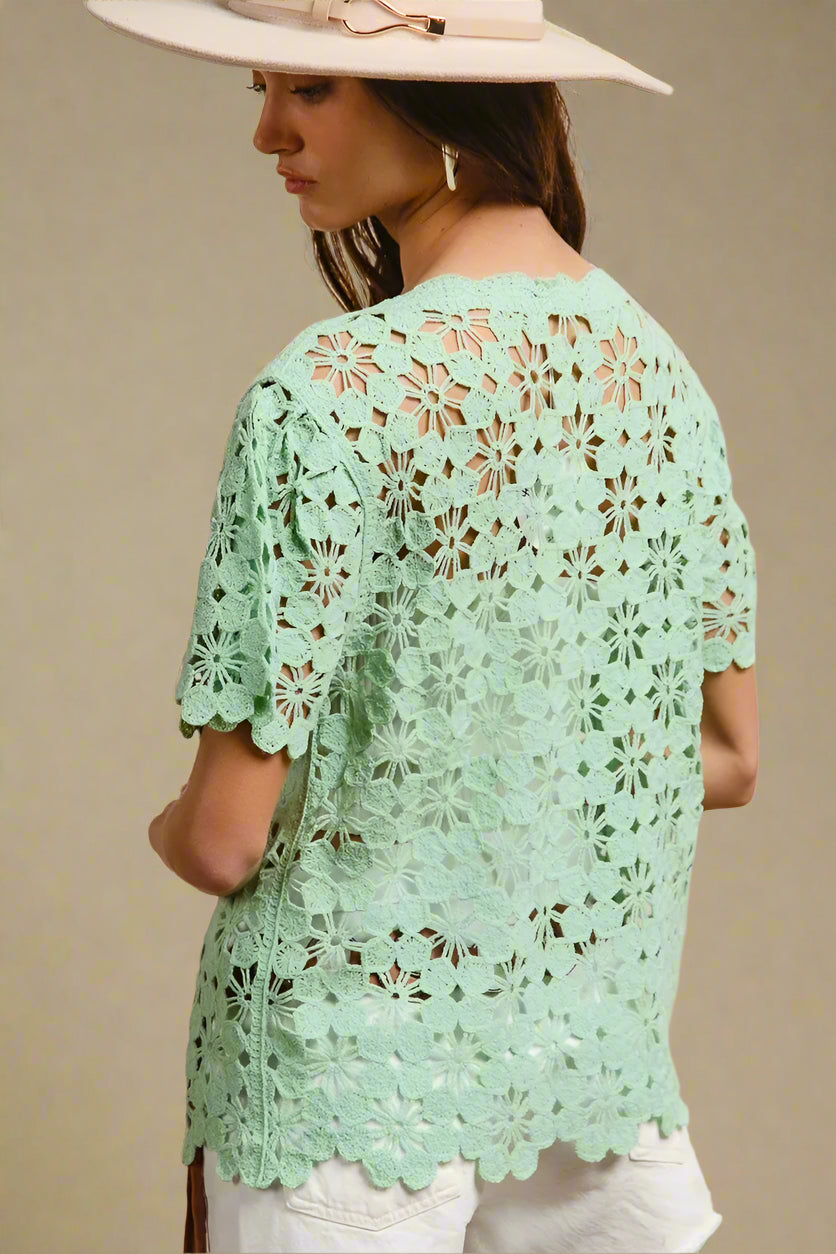 Woman wearing a light green crochet top with a beige background