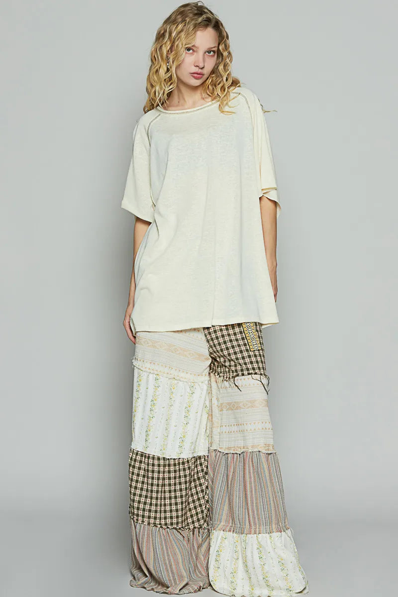 Woman wearing a light-colored top and patchwork pants against a plain background