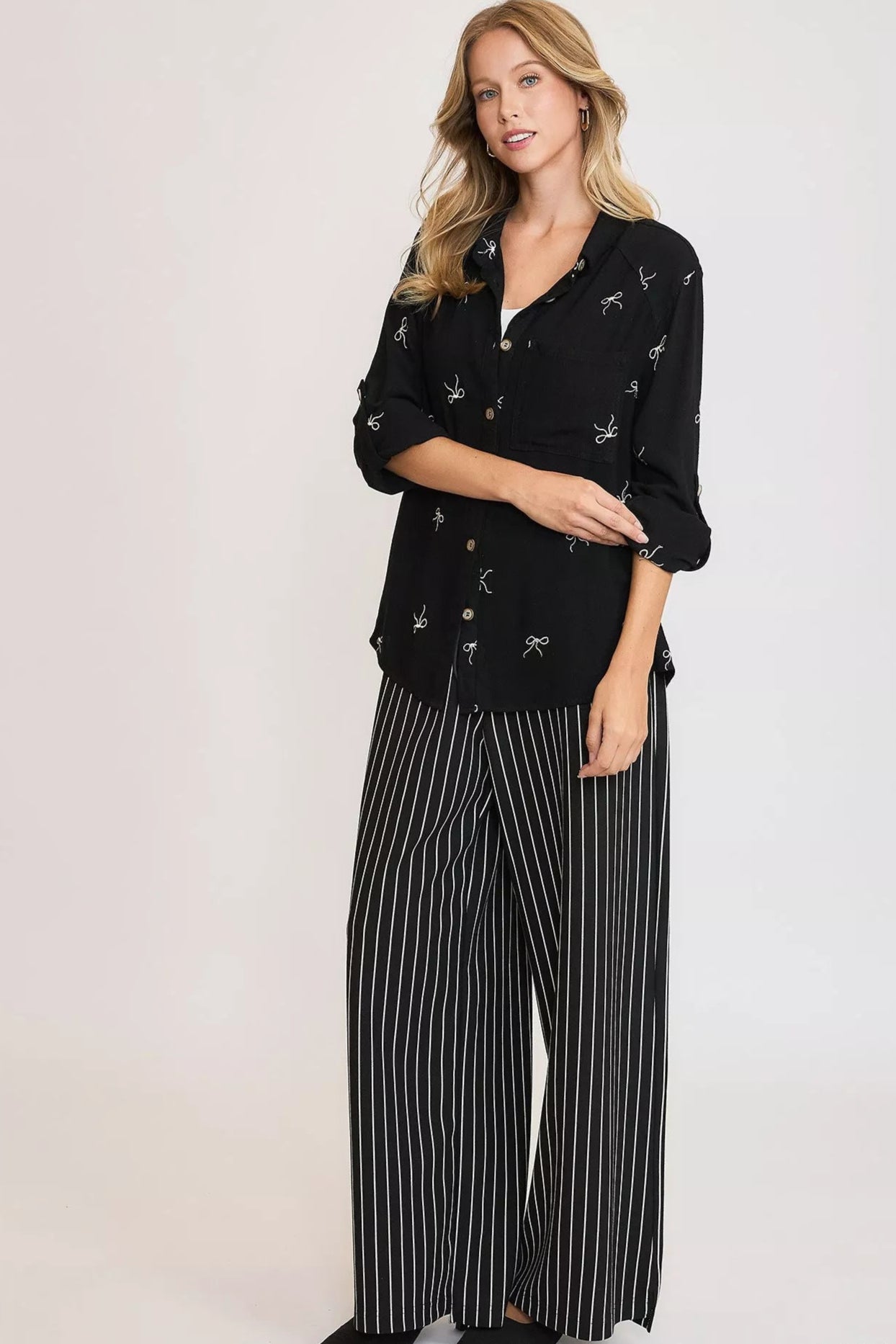 Woman wearing a black patterned top and striped pants on a white background