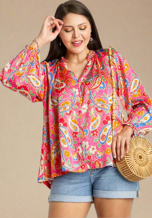 Woman wearing a colorful paisley blouse and denim shorts, holding a wooden clutch.