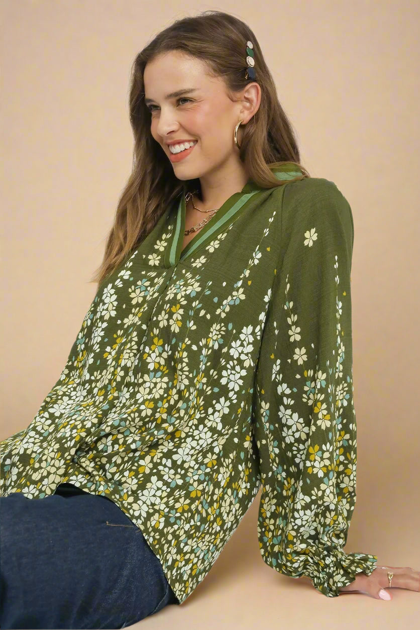 Woman wearing a green floral blouse sitting on a beige surface
