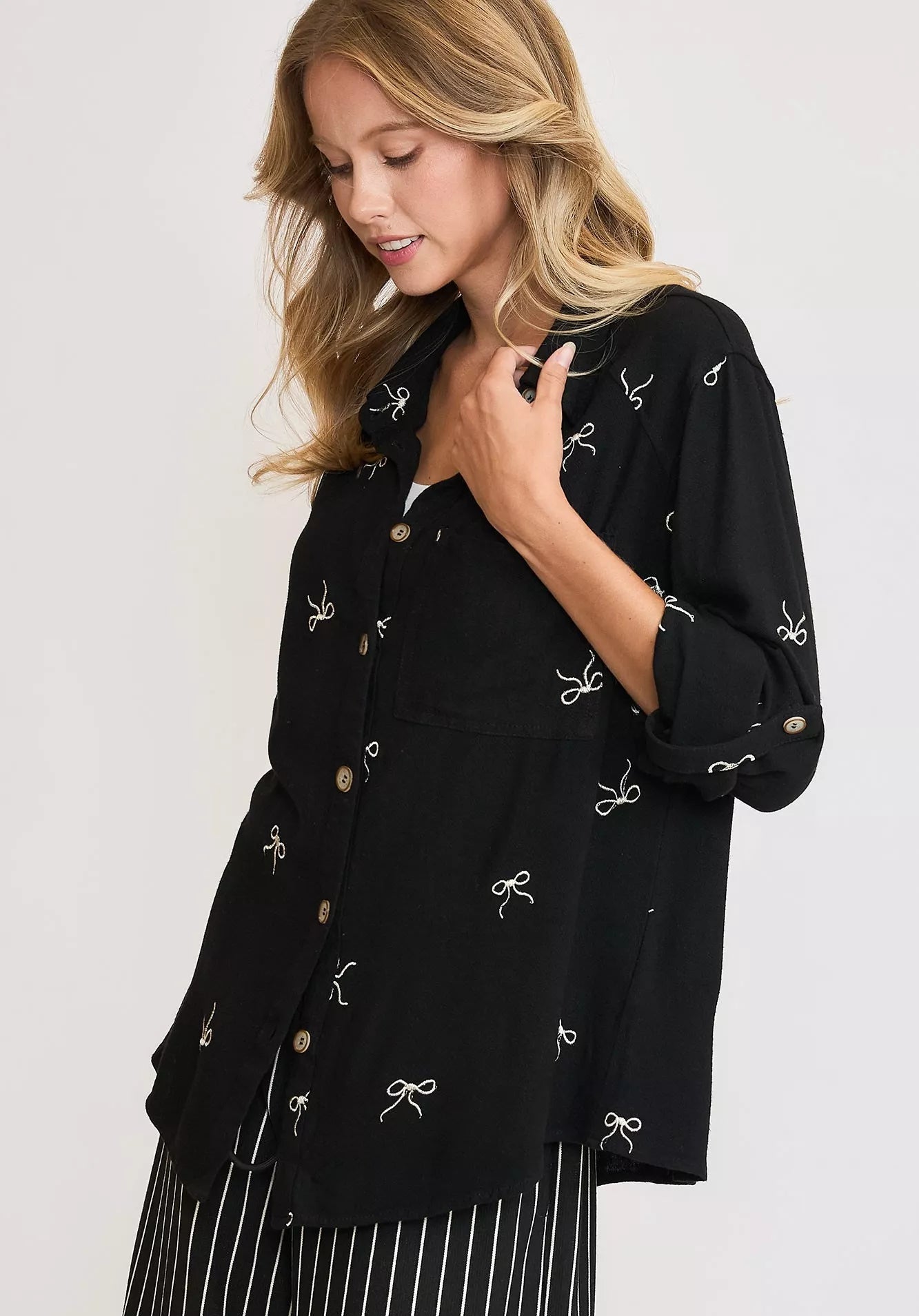 Woman wearing a black blouse with white bow patterns on a light gray background