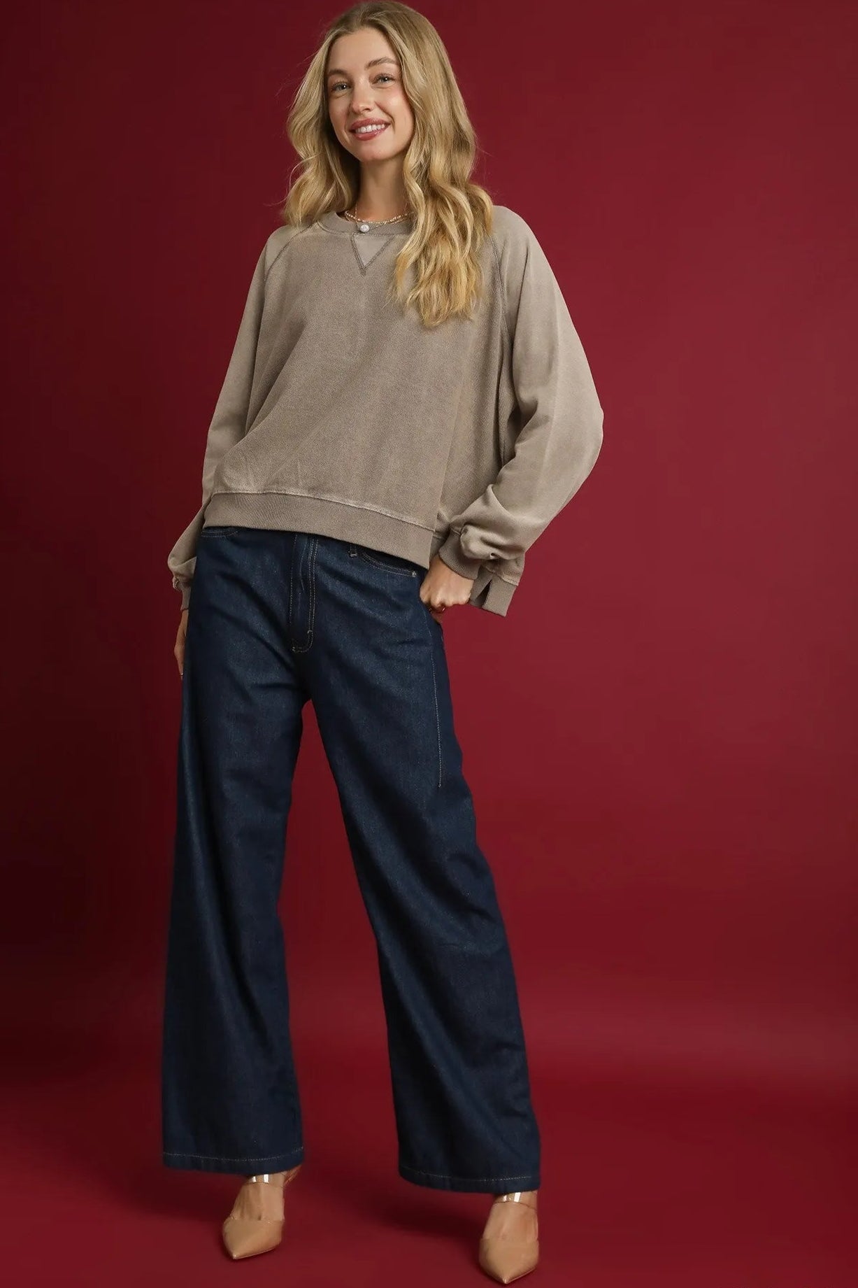 Woman wearing a beige sweater and navy pants on a red background