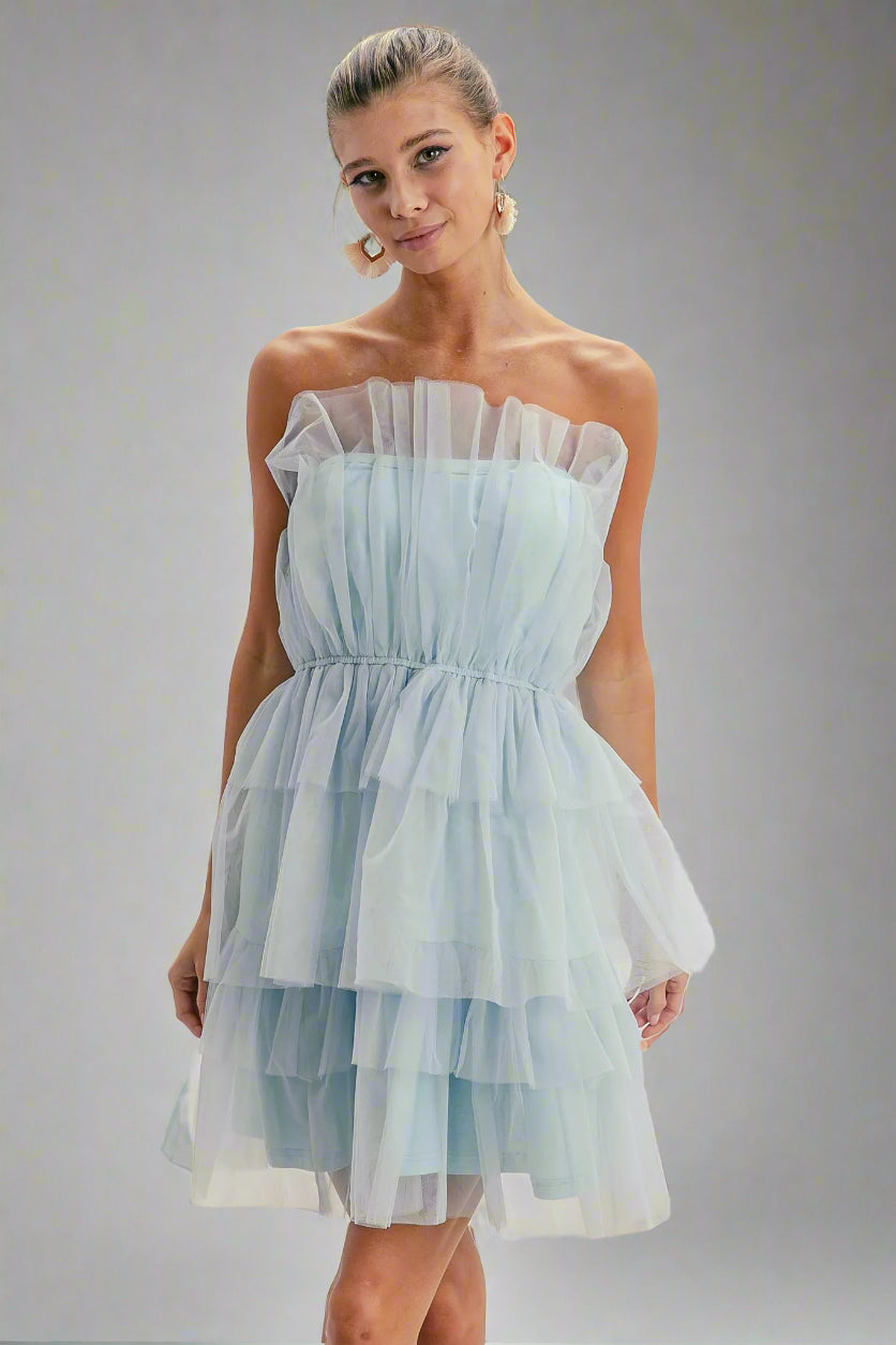 Woman wearing a light blue strapless dress in a minimal indoor setting.