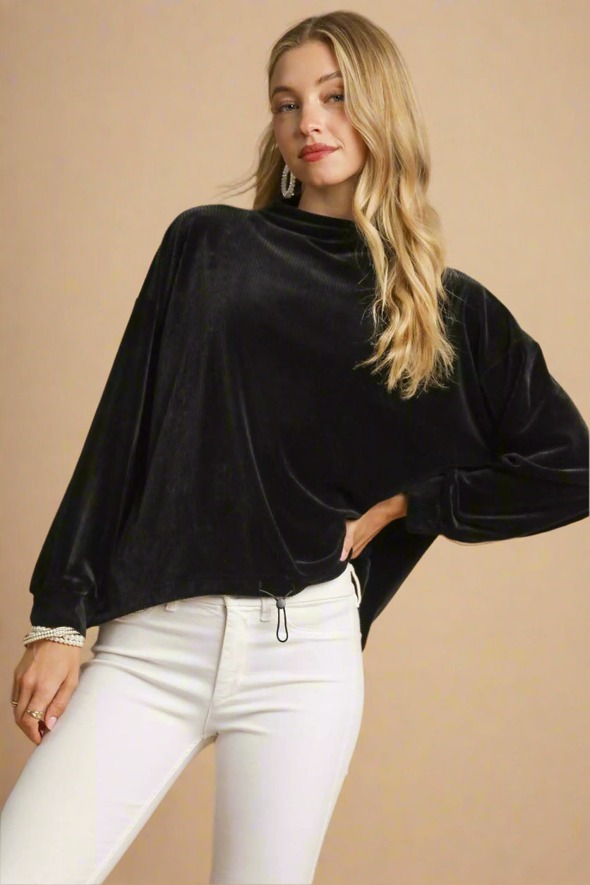 Woman wearing a black velvet top and white pants on a beige background