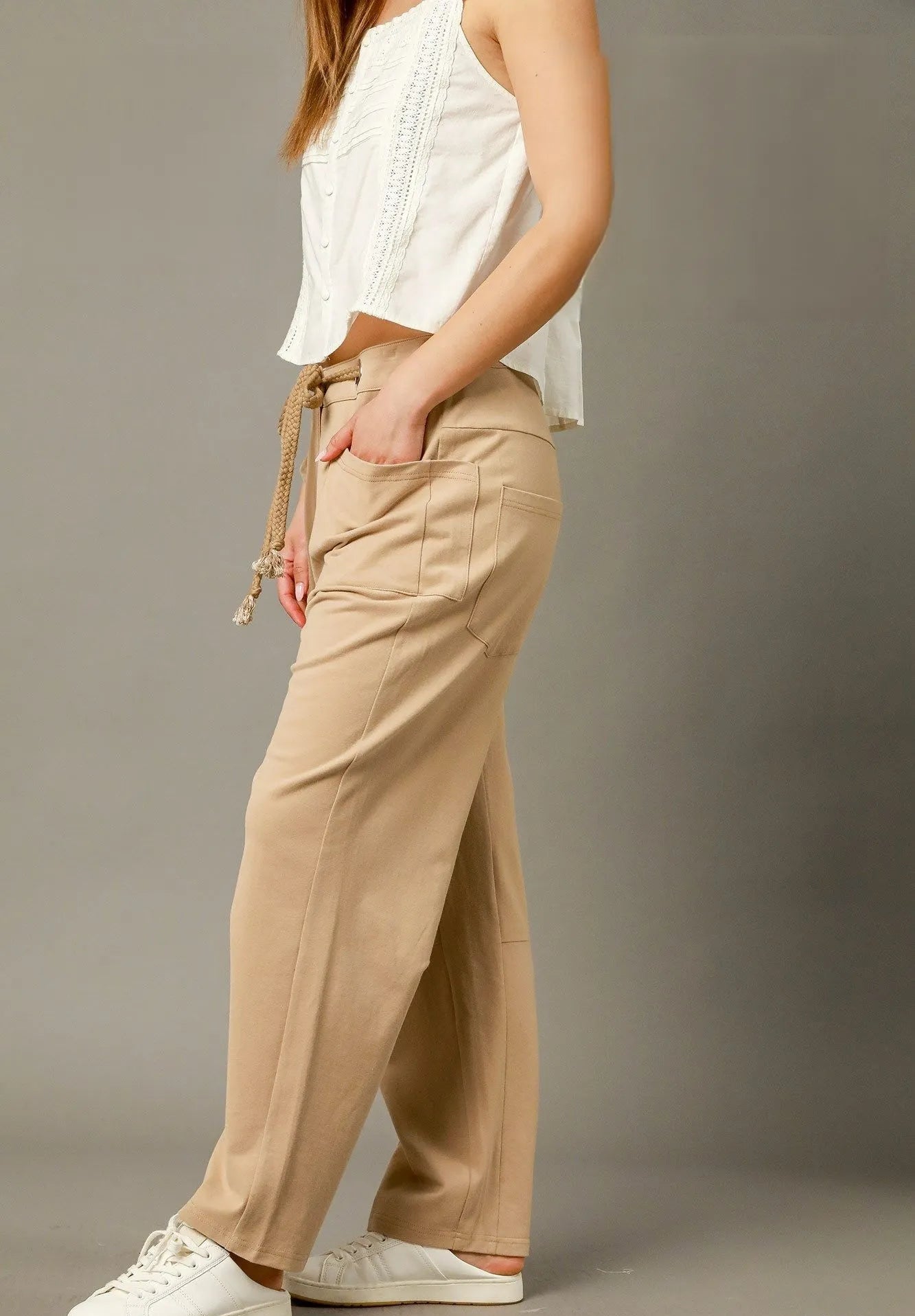 Person wearing beige pants and a white top on a gray background