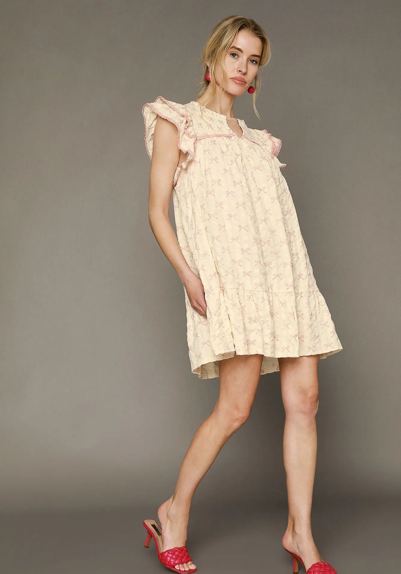 Woman wearing a light-colored dress with ruffled sleeves against a gray background