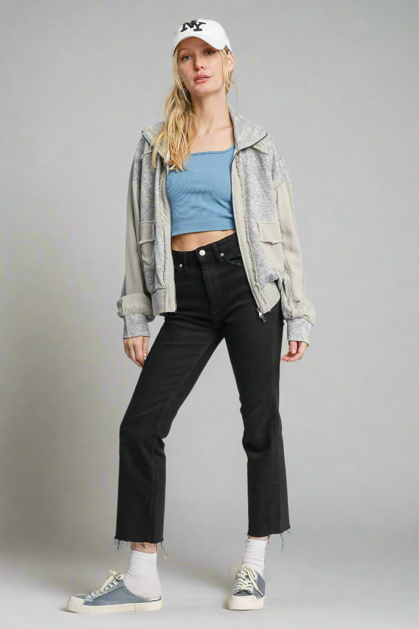 Woman wearing a blue top, black pants, and a gray jacket on a white background