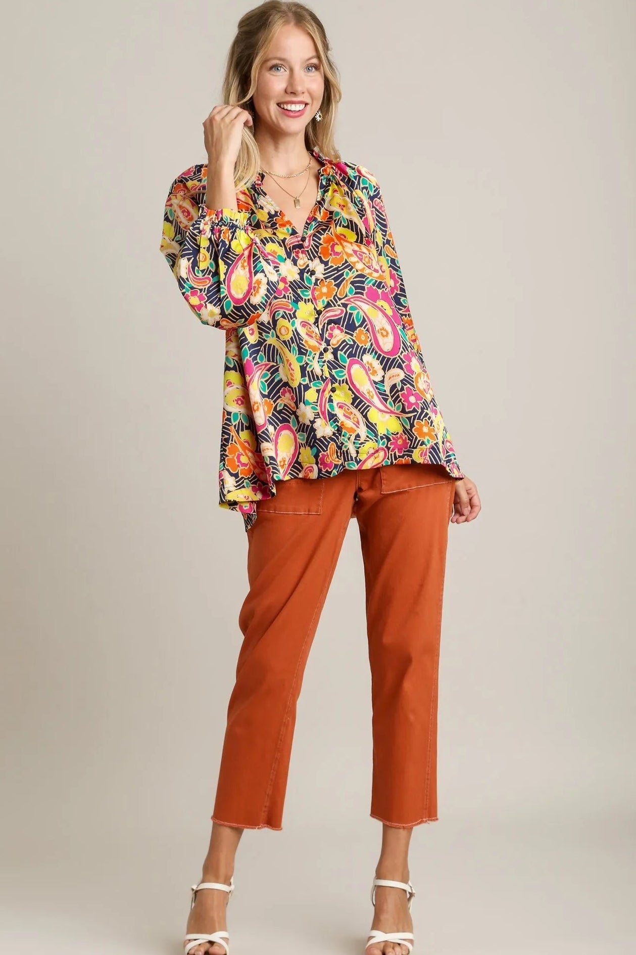 Woman wearing a colorful patterned blouse and rust-colored pants on a beige background