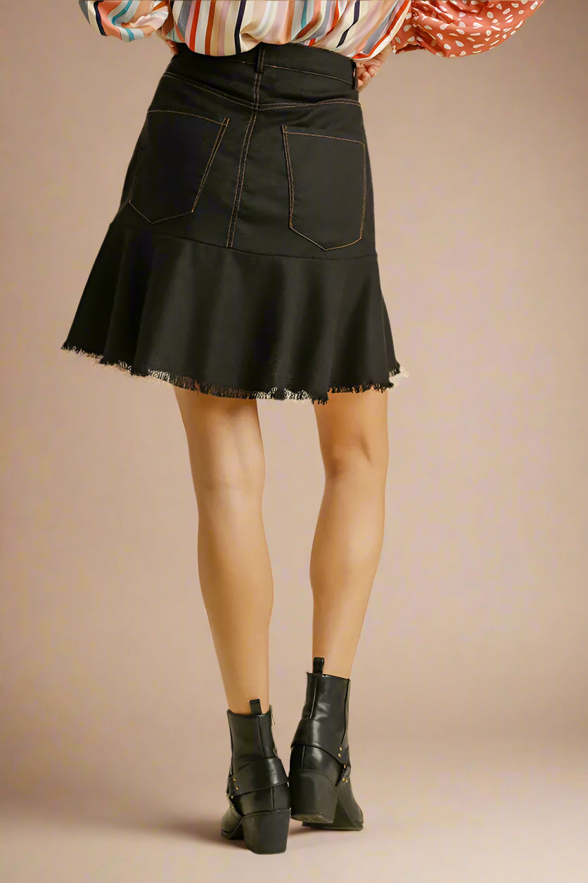 Black denim skirt worn with a colorful top and black boots on a beige background