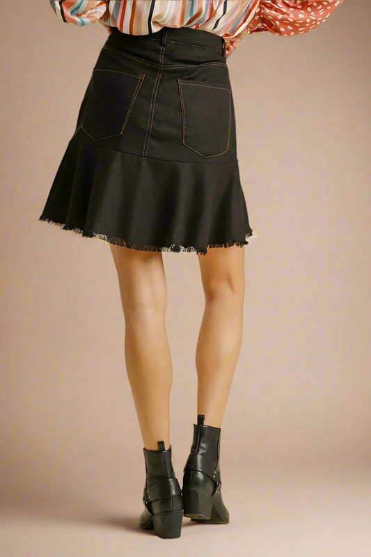 Black denim skirt worn with a colorful top and black boots on a beige background