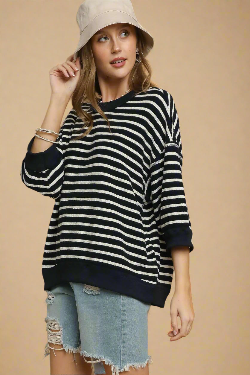 Woman wearing a black and white striped sweater with rolled-up sleeves and denim shorts on a brown background.