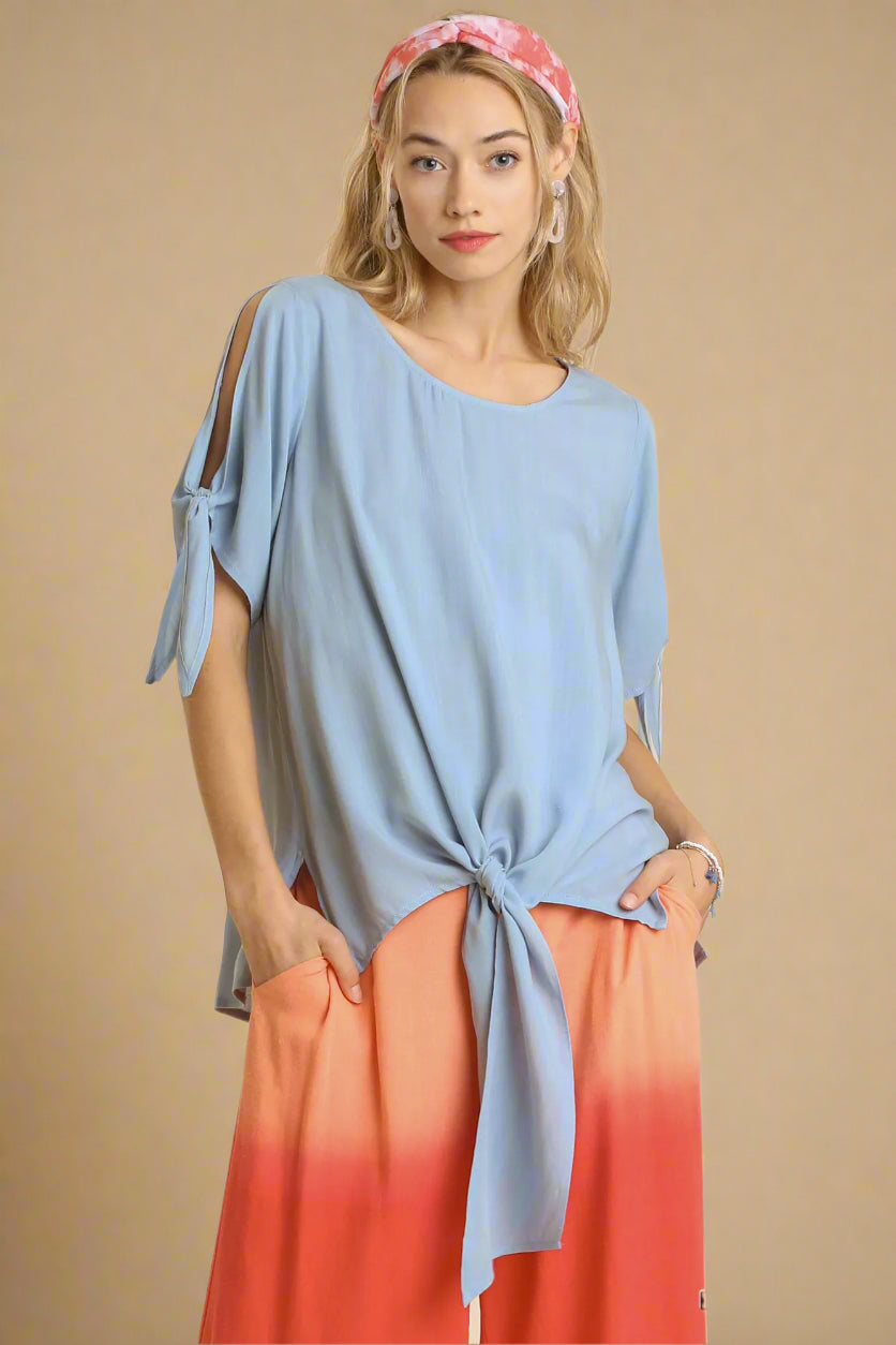 Woman wearing a light blue top with tied sleeves and an ombre orange skirt on a beige background