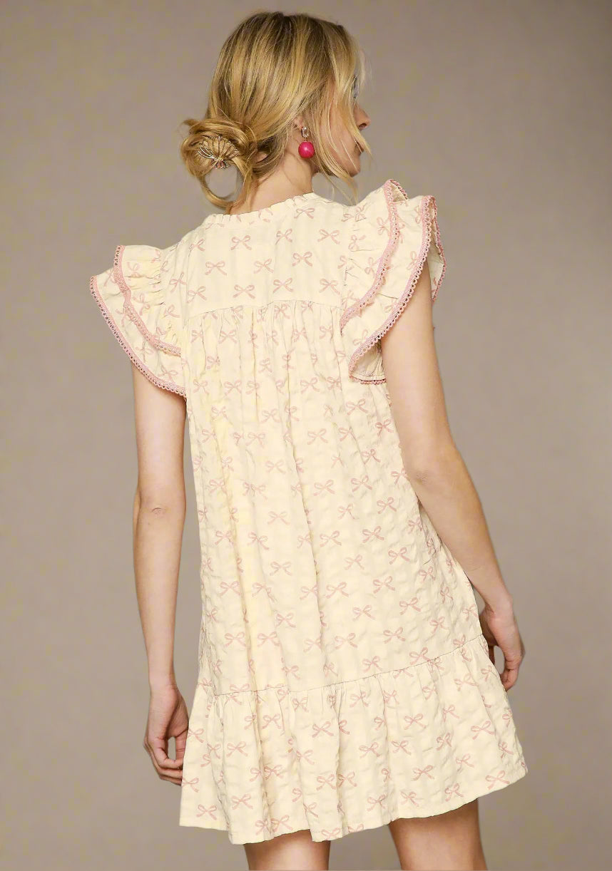 Woman wearing a light pink dress with ruffled sleeves against a beige background