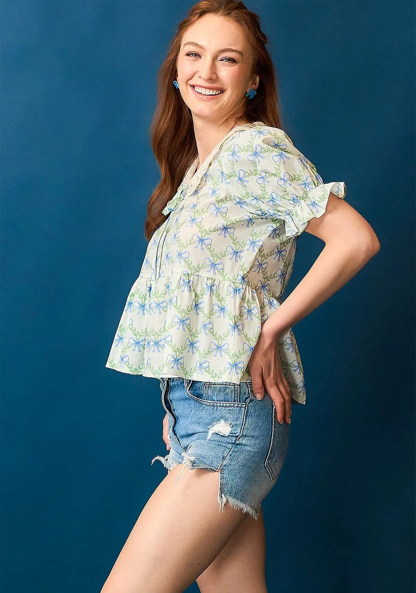 Woman wearing a floral top and denim shorts against a blue background