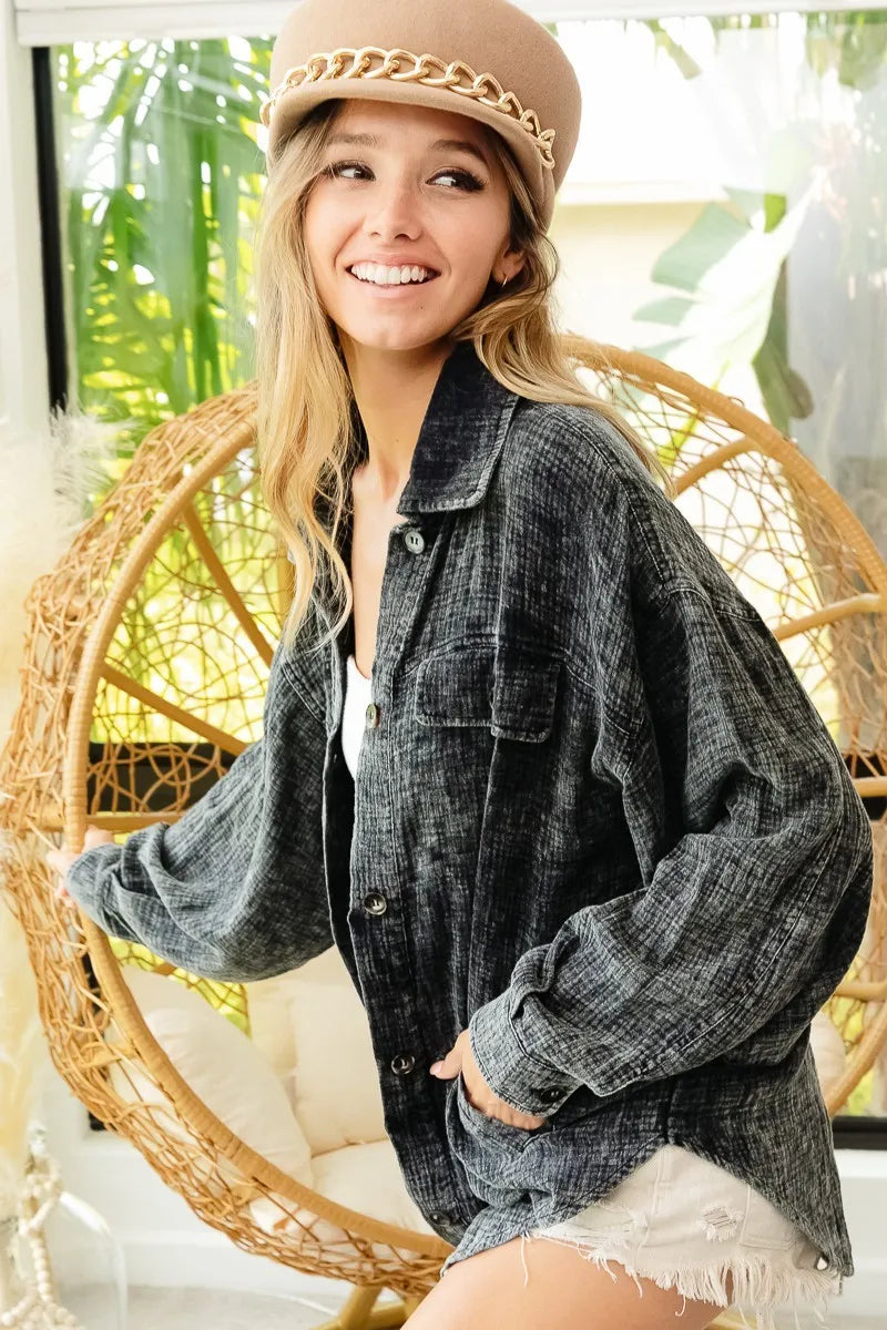 Woman wearing a denim jacket and beige hat sitting on a wicker chair with greenery in the background