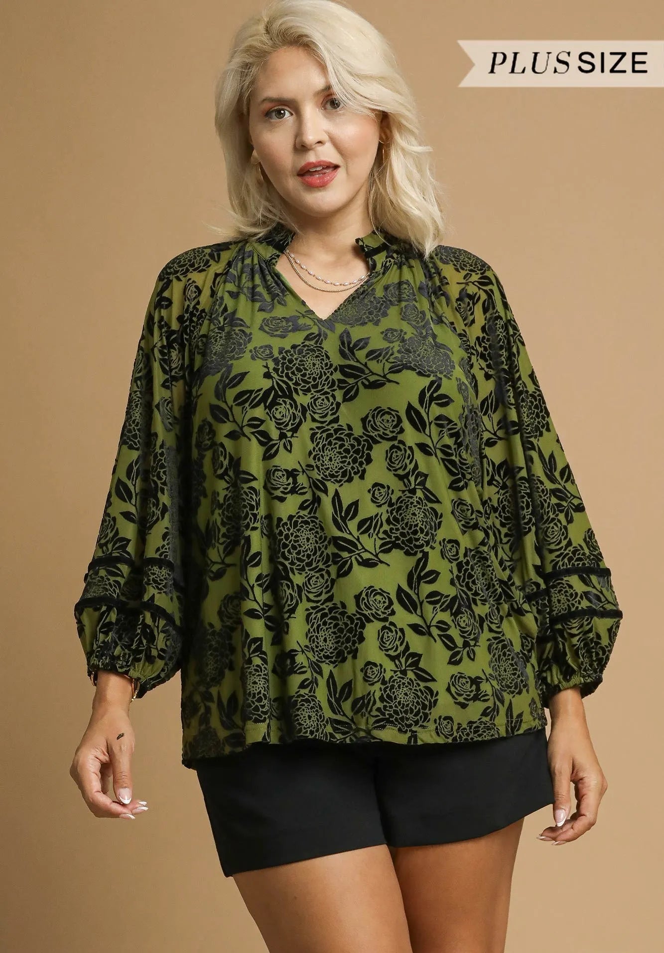 Woman wearing a green floral blouse with black patterns on a beige background