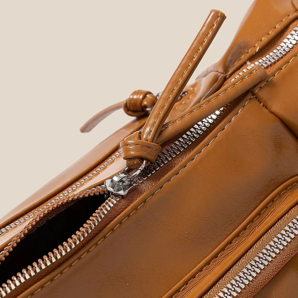 Close-up of a brown leather bag with zippers on a beige background