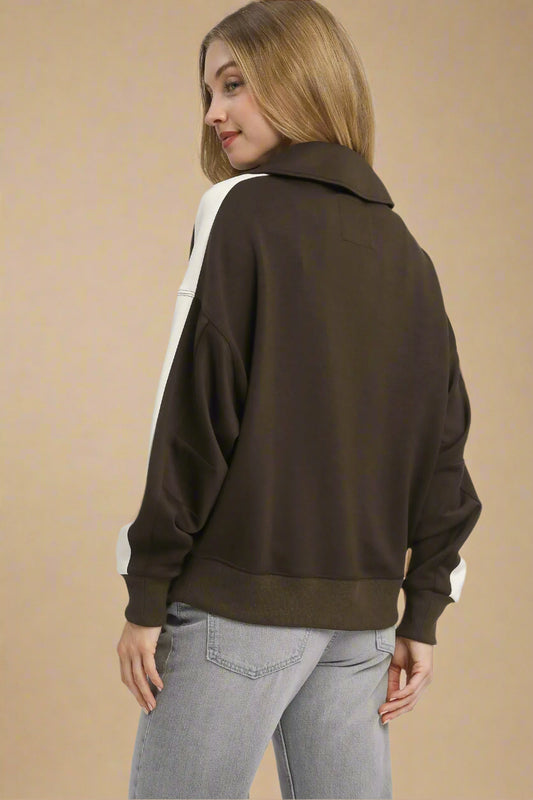 Woman wearing a brown sweater with a white shirt underneath on a light gray background