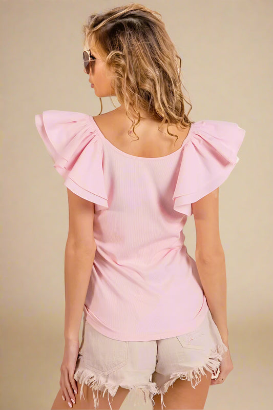 Woman wearing a pink top with ruffled sleeves on a beige background