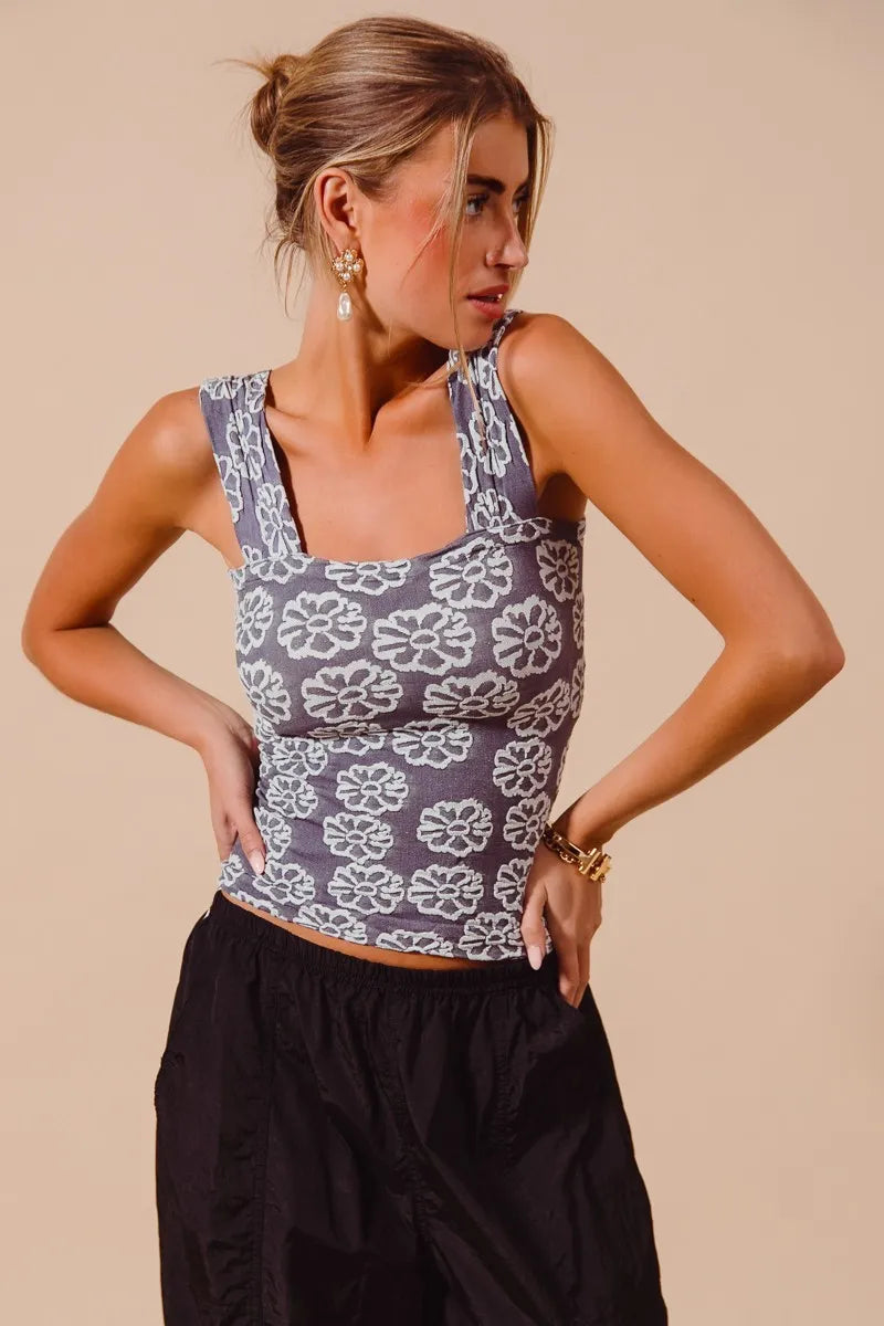 Woman wearing a floral sleeveless top and black pants against a beige background