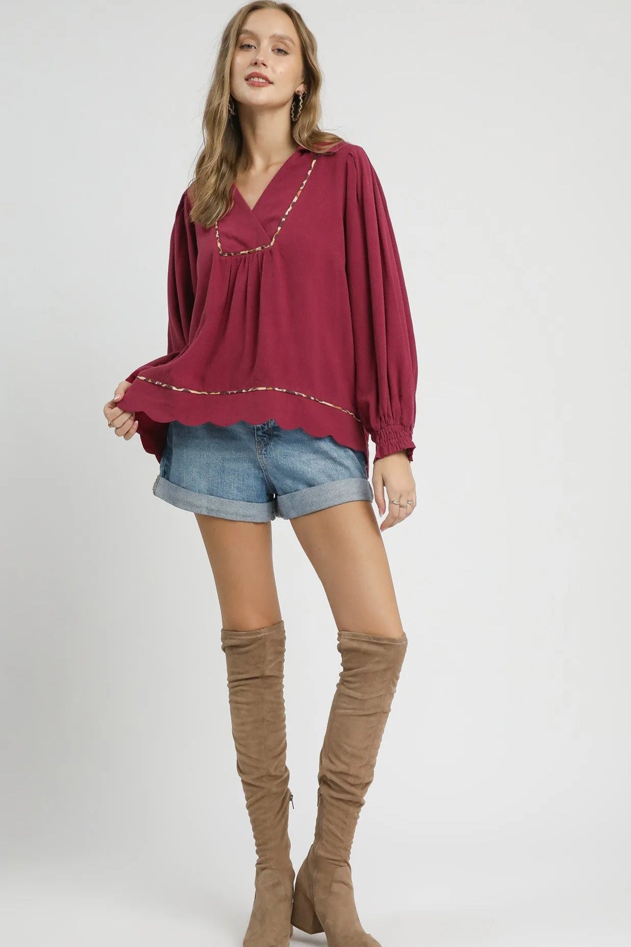 Woman wearing a burgundy top and denim shorts with brown knee-high boots on a white background