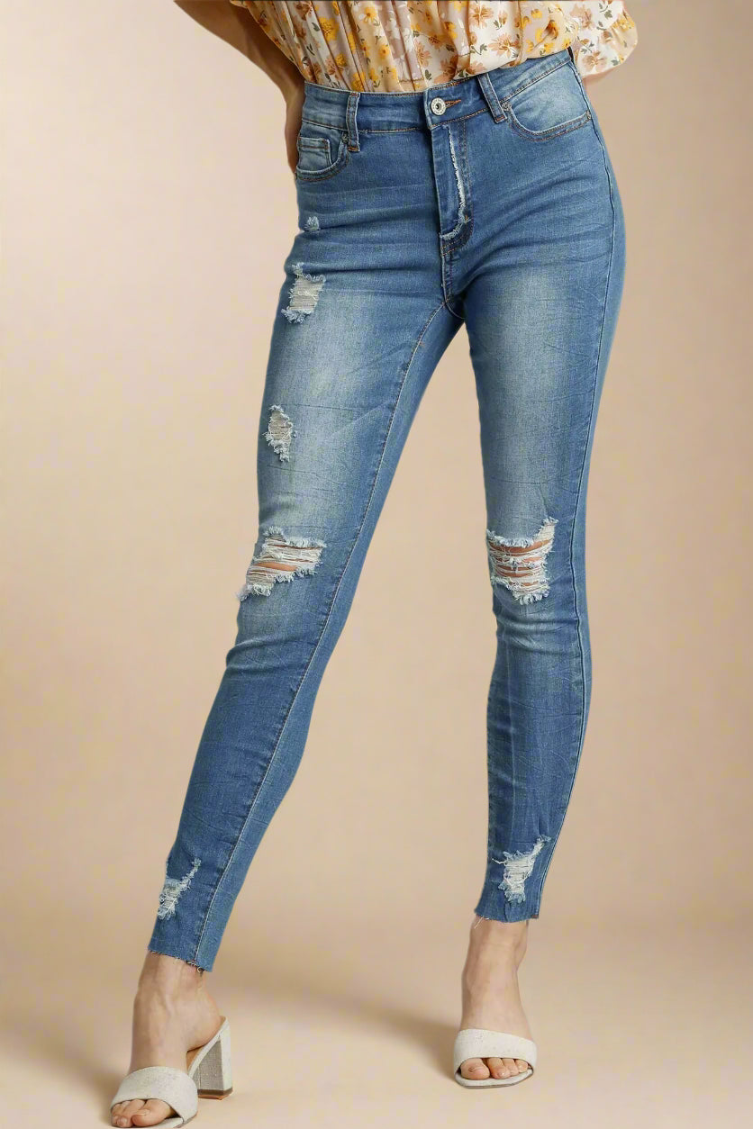 Blue distressed jeans worn by a person on a beige background