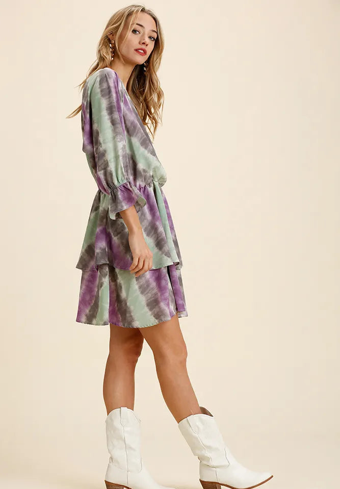 Woman wearing a green and purple tie-dye dress with white cowboy boots on a beige background