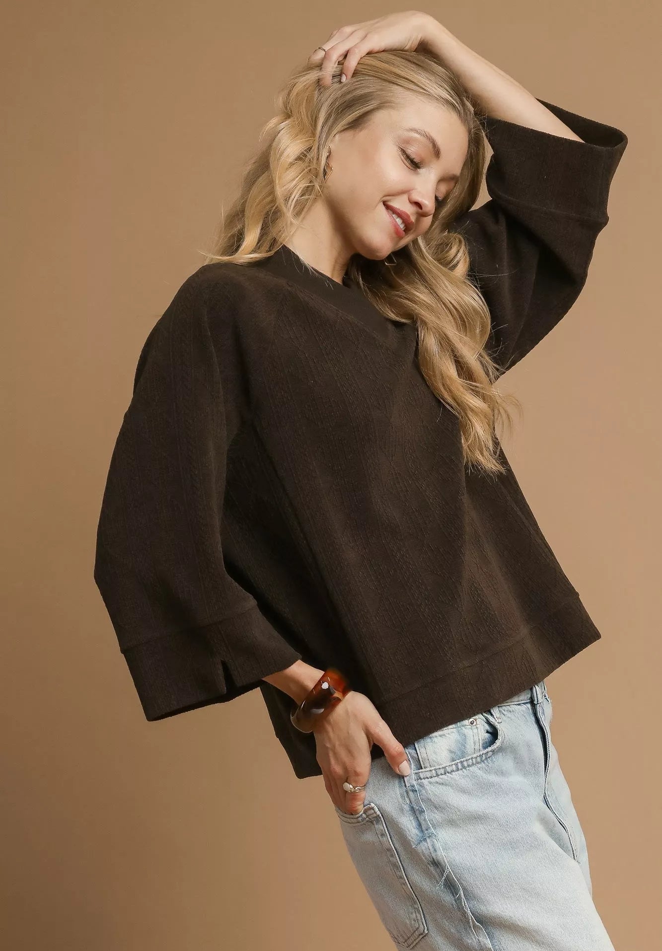 Woman wearing a brown sweater and light blue jeans against a beige background