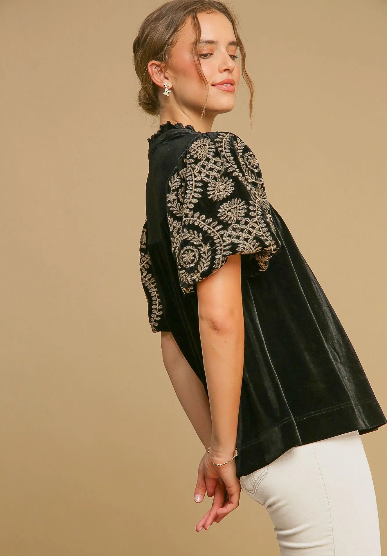 Woman wearing a black top with gold embroidery on a beige background
