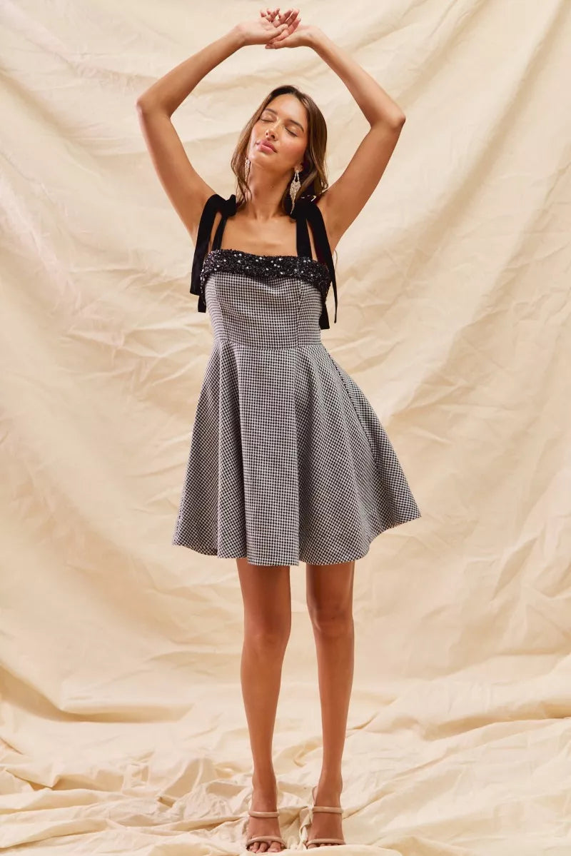 Woman wearing a checkered dress with a black top against a beige background