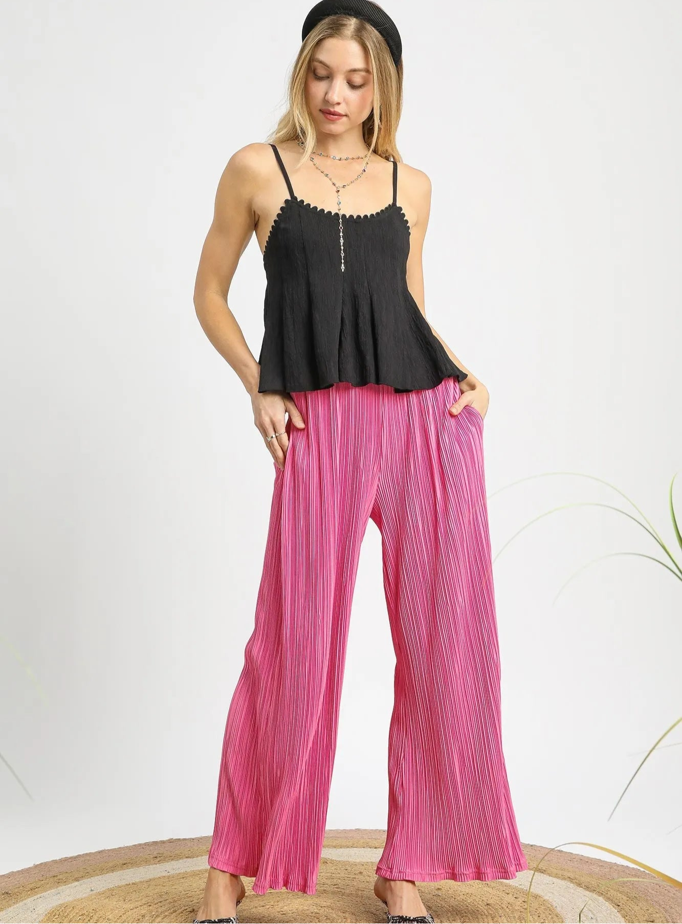 Woman wearing a black top and pink pleated pants on a white background