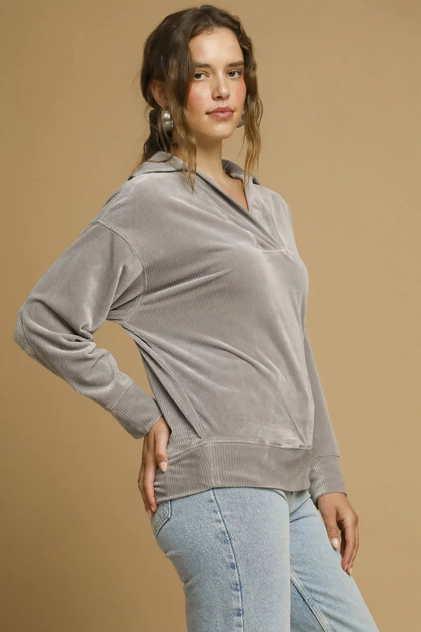 Woman wearing a gray long-sleeve top and light blue jeans against a beige background