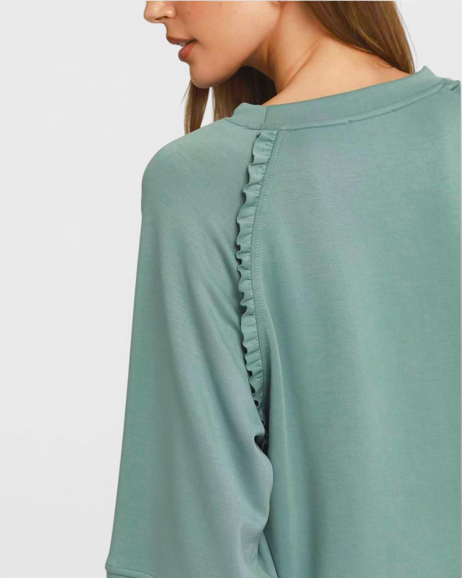Green long-sleeve top with ruffled details on a plain background