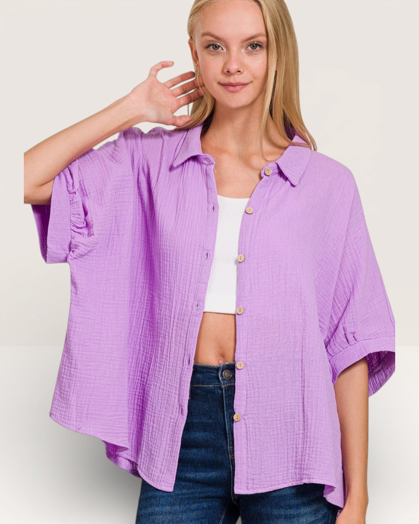 Woman wearing a purple shirt over a white top with blue jeans on a plain background
