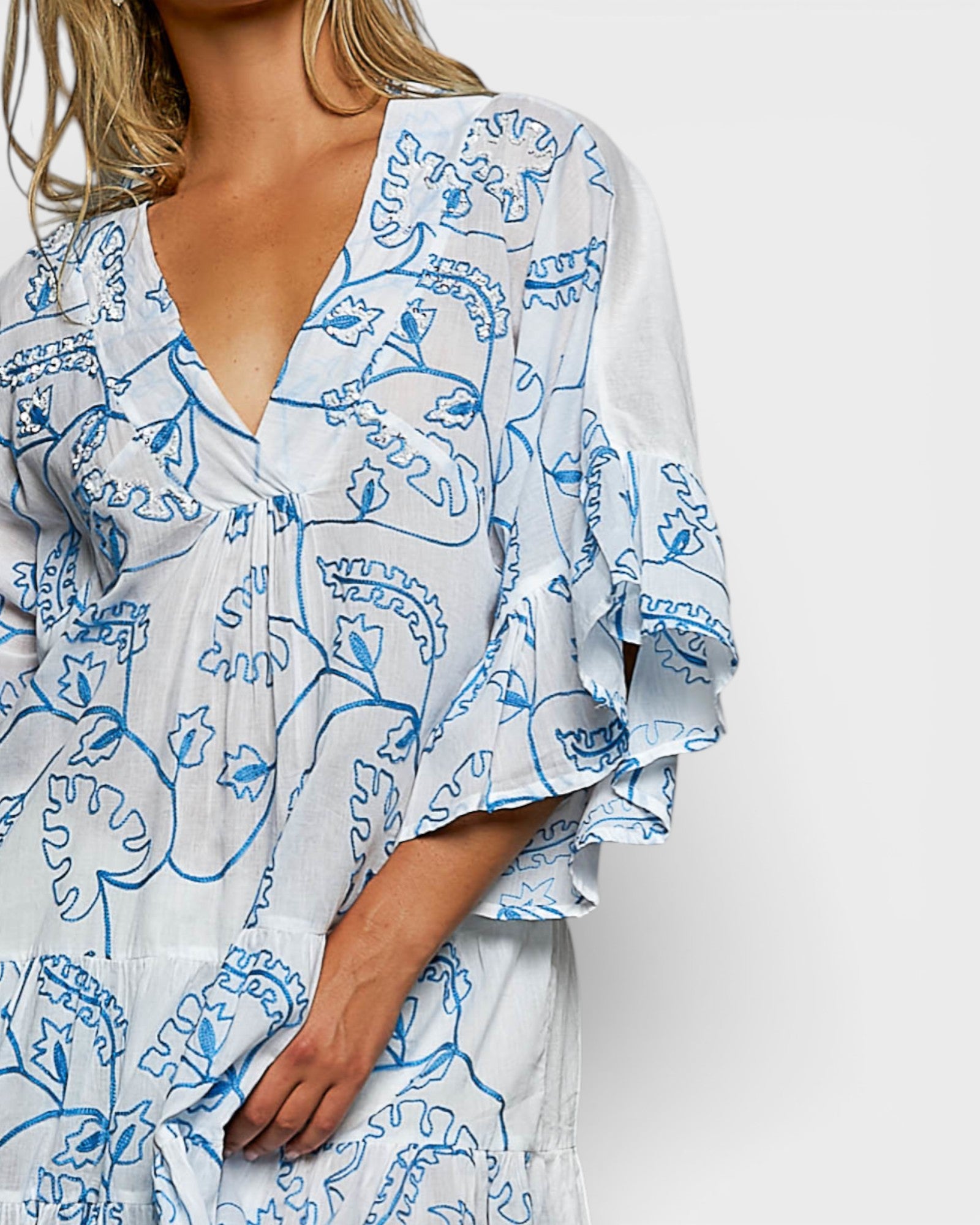 Woman wearing a white dress with blue floral patterns on a plain background