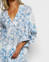 Woman wearing a white dress with blue floral patterns on a plain background