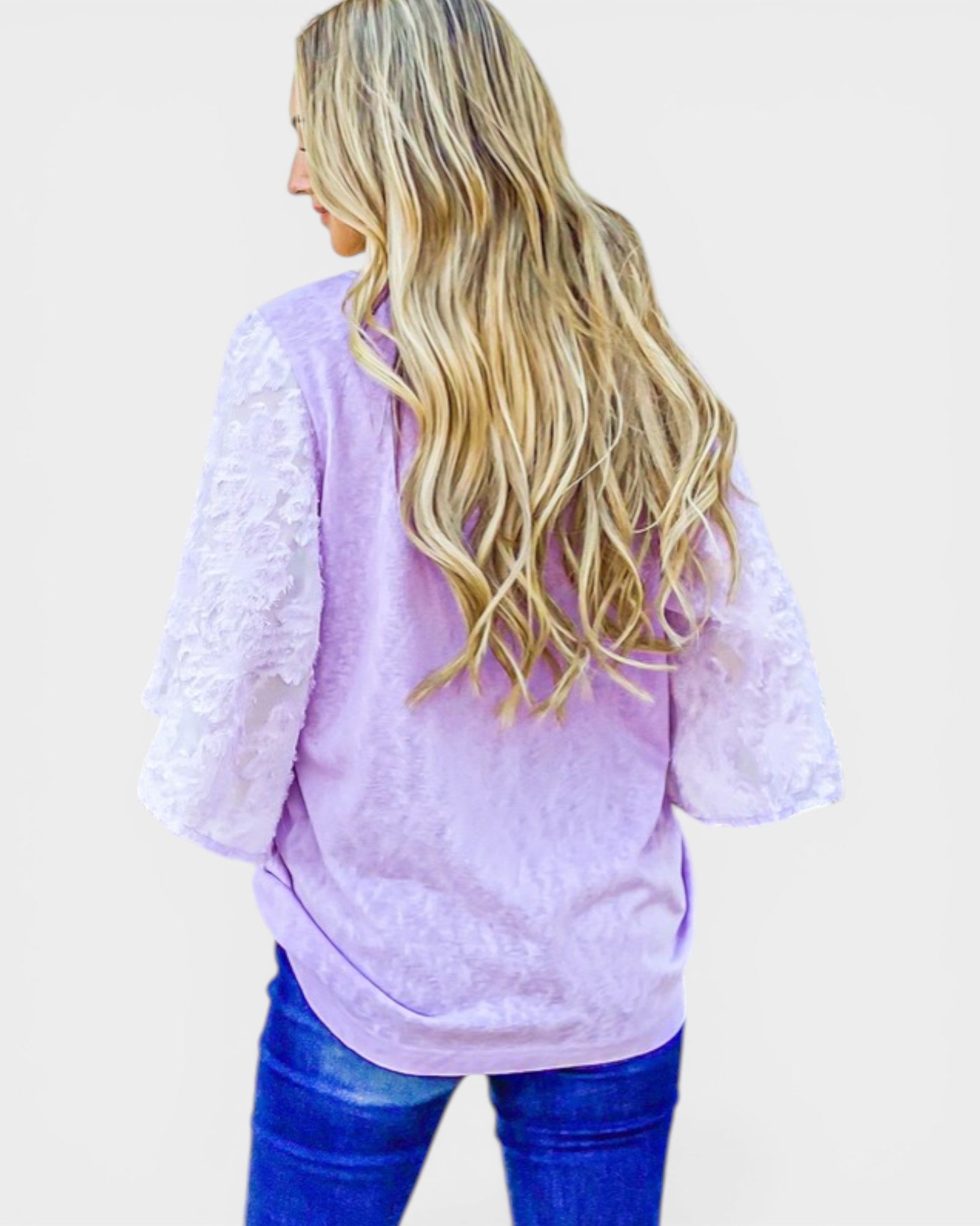 Person wearing a light purple lace top with blue jeans on a plain background