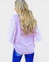 Person wearing a light purple lace top with blue jeans on a plain background