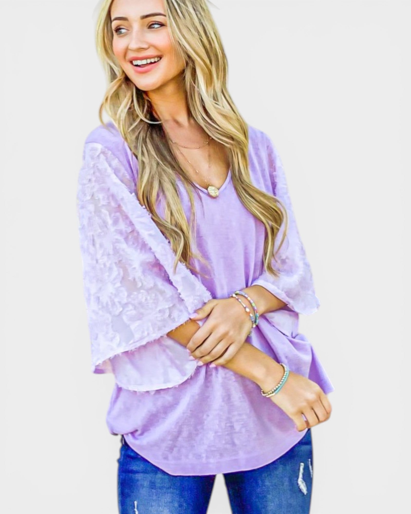 Woman wearing a light purple lace top and jeans on a plain background