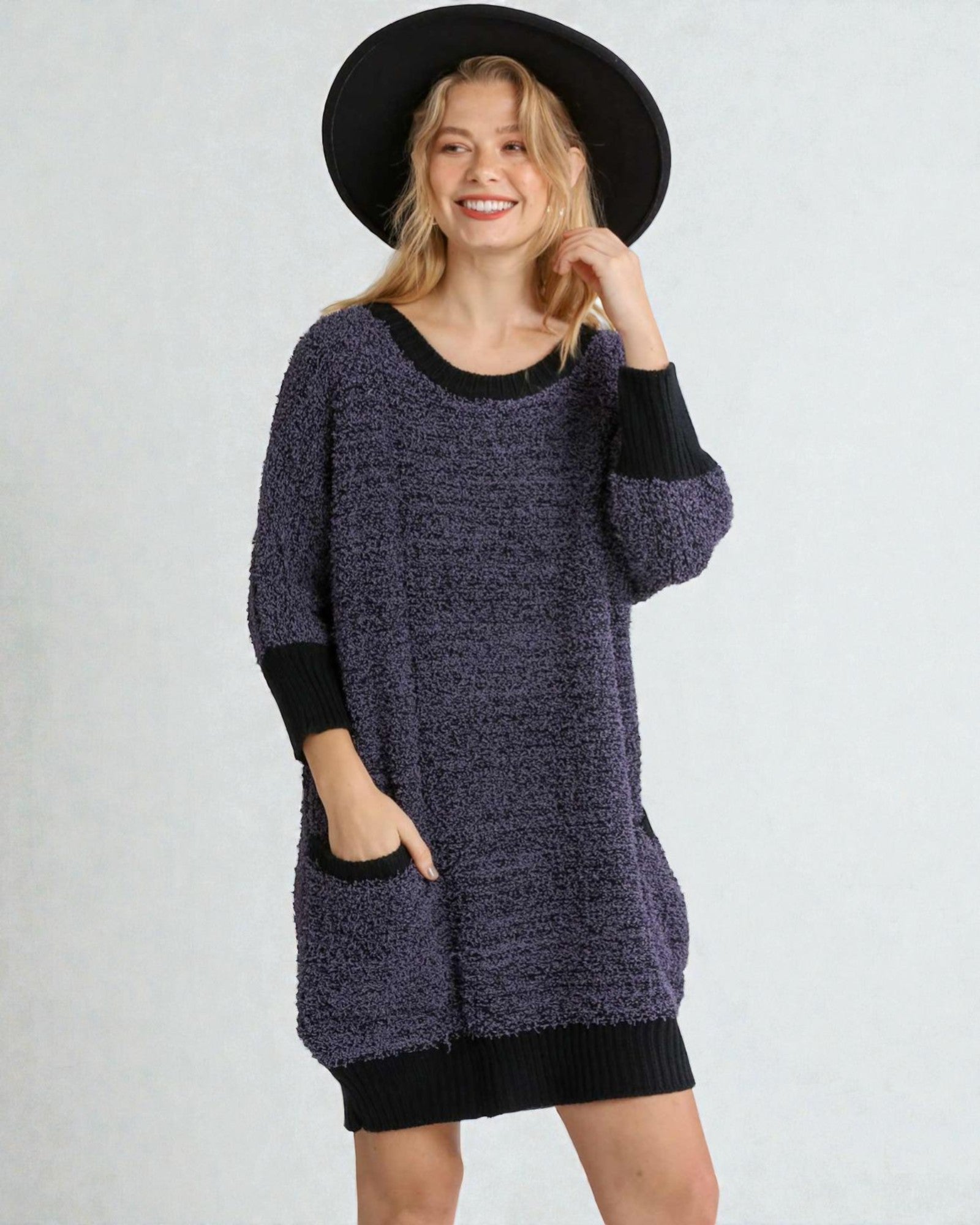 Woman wearing a dark blue knitted sweater with black cuffs and a black hat on a white background