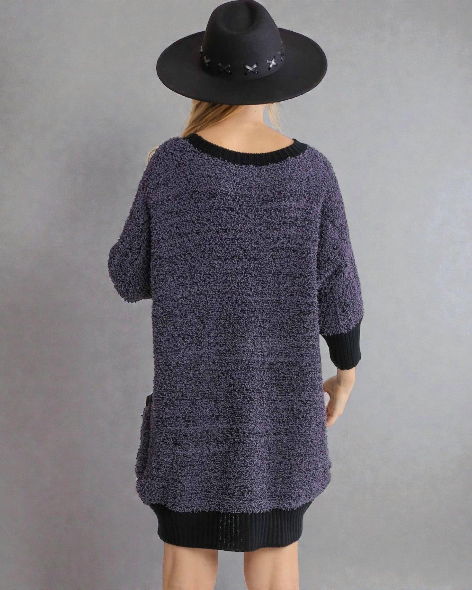 Person wearing a dark textured sweater and black hat on a gray background
