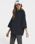 A woman wearing a navy blue oversized pullover hoodie with wide three-quarter sleeves, paired with gray leggings and a white baseball cap with a black 'NY' logo, set against a plain light gray background.