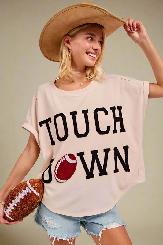 Woman wearing a 'Touchdown' t-shirt with a football graphic, holding a football and a hat.