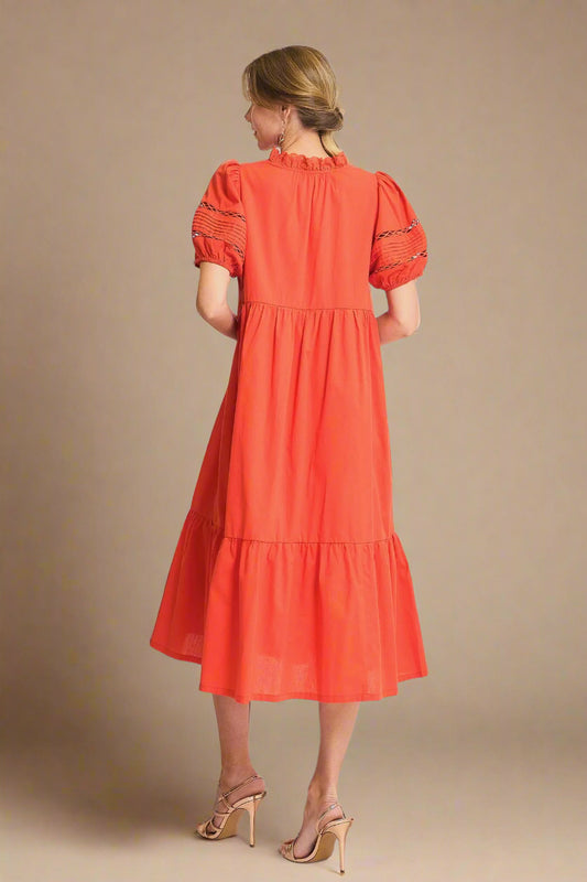 Woman wearing a tomato red dress with puff sleeves on a light background