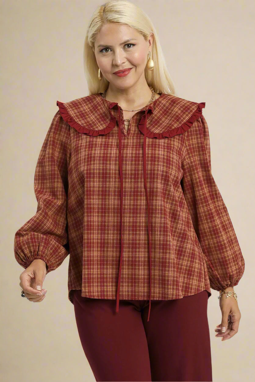 Woman wearing a rust-colored plaid blouse with a ruffled collar on a beige background